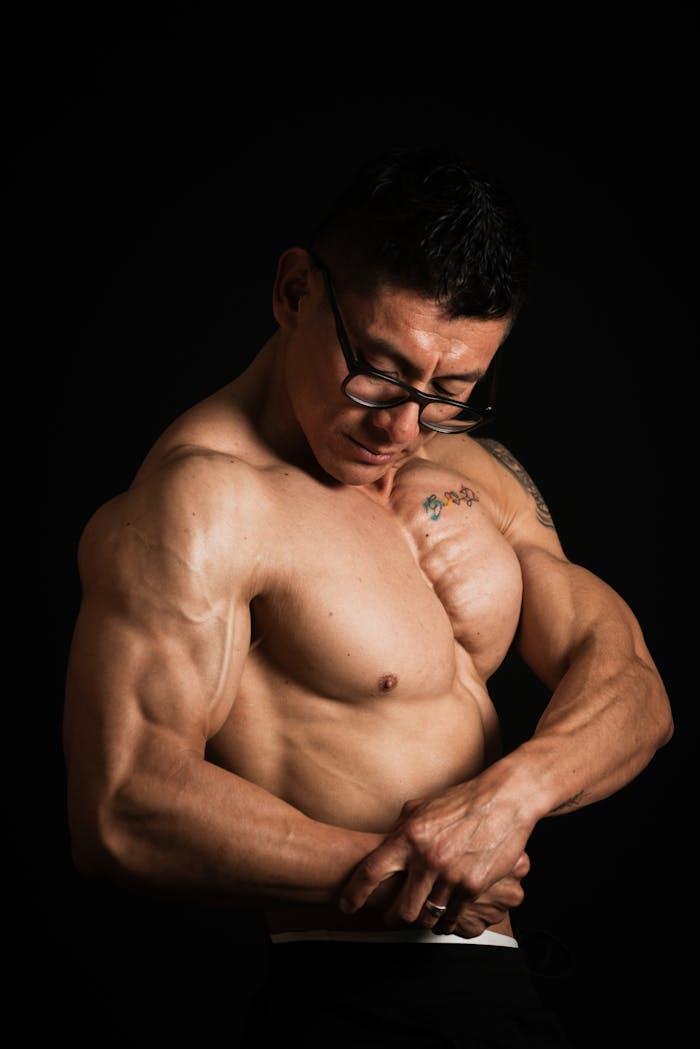 Shirtless man flexing muscles in studio against a black background.